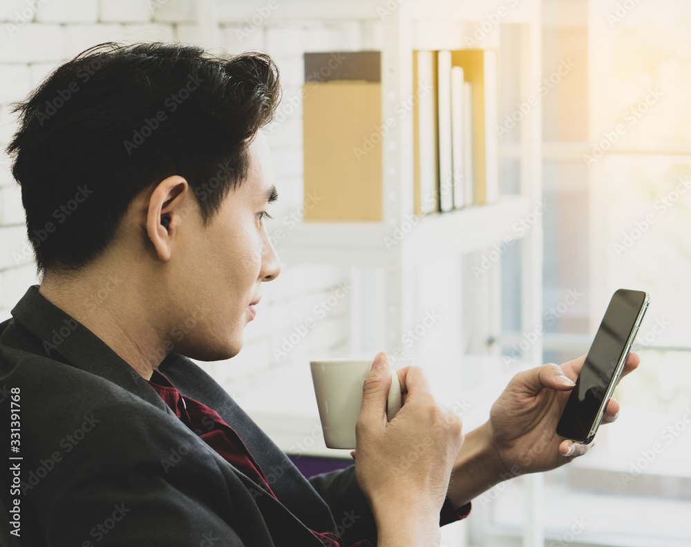 A young asian businessman with confident face sitting onthe chair using smart phone in the office in day time A young asian businessman with confident face sitting onthe chair using smart phone in the office in day time