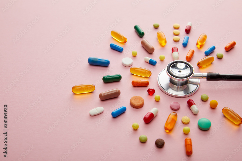 High angle view of stethoscope with bright colorful pills on pink background High angle view of stethoscope with bright colorful pills on pink background