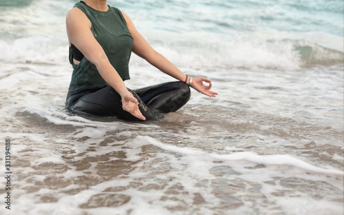 Young Woman Doing Yoga at the Ocean, the wave covered her. Attractive Woman in Sportswear Relaxing Outdoor. Health People Concept. Copy Space