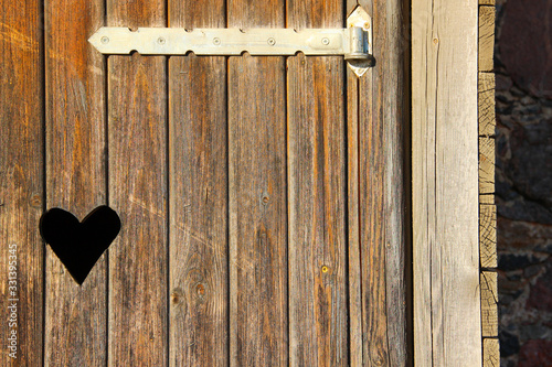 Old-fashioned toilet door with carved heart shape. Weathered wooden door with a heart-shaped peephole.