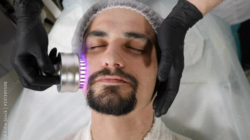 Top view on Young handsome man getting cosmetology procedure in beauty salon. Hardware cosmetology. Anti-aging and anti-wrinkle apparatus cosmetology. Modern relaxing treatment. 4 k footage Top view on Young handsome man getting cosmetology procedure in beauty salon. Hardware cosmetology. Anti-aging and anti-wrinkle apparatus cosmetology. Modern relaxing treatment. 4 k footage