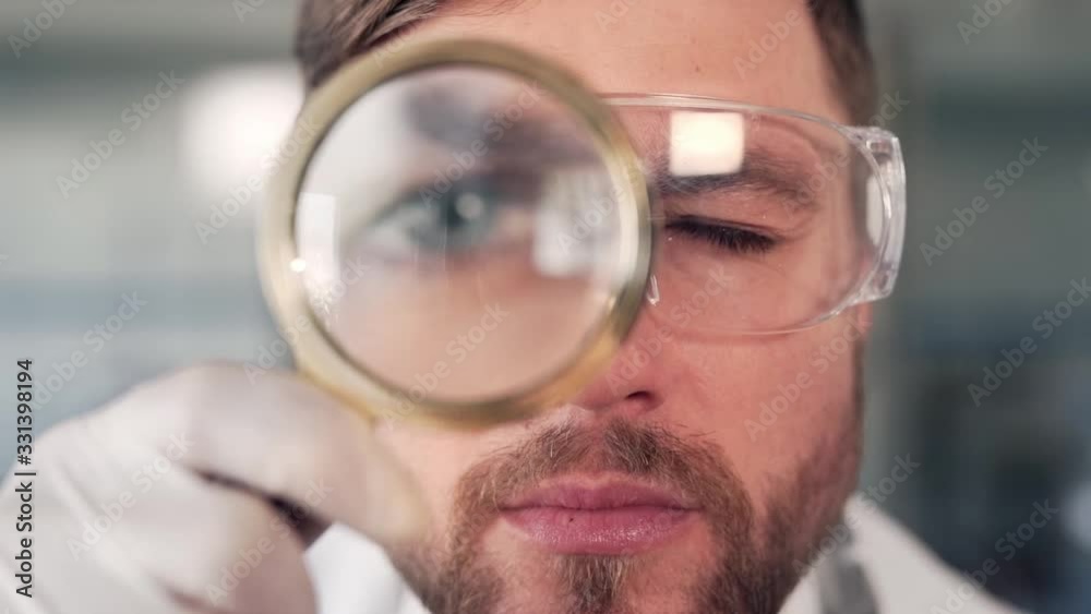 closeup portrait of male doctor scientist in glasses with magnifier looks carefully at camera lens closeup portrait of male doctor scientist in glasses with magnifier looks carefully at camera lens