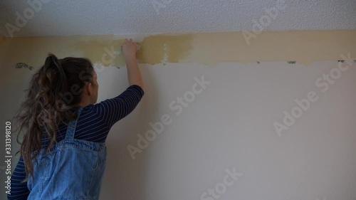 Young Woman scrubs wallpaper border residue off of white walls photo