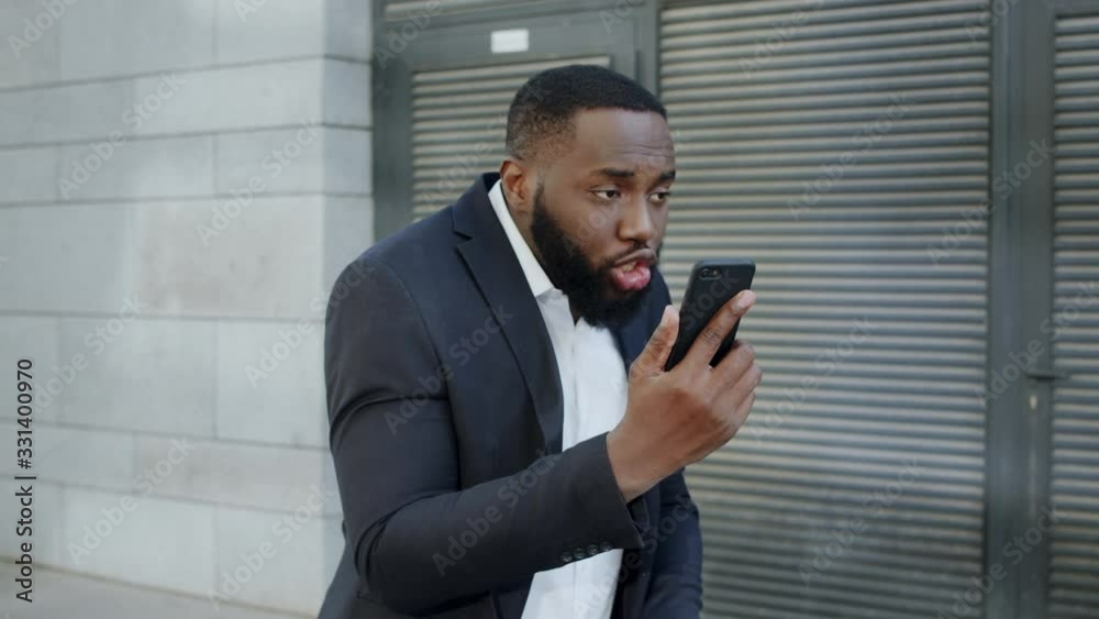 Afro businessman yelling on camera at street. Manager using smartphone outdoors Afro businessman yelling on camera at street. Manager using smartphone outdoors