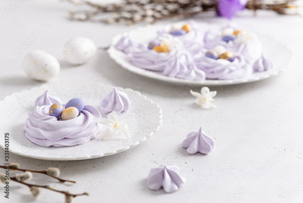 Easter bird nest meringue cookies - lilac mini Pavlova desserts with pastel candy eggs in nest shape for Easter holiday party. Side view, close up. Confectionery, bakery concept, greeting card
