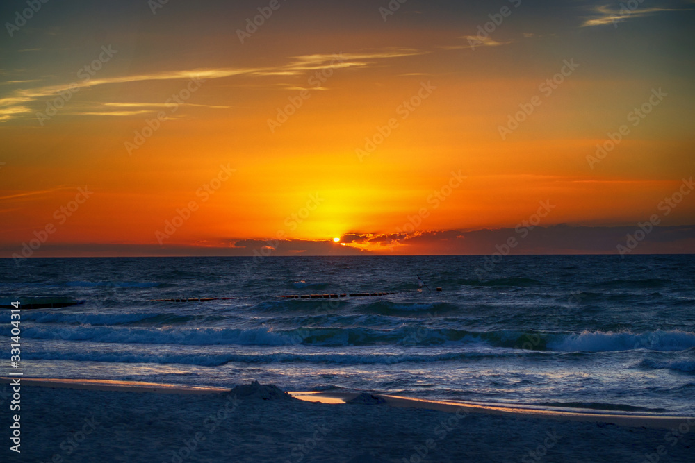 Sonnenuntergang an einem verlassenen Strand der Ostsee mit Meereswellen vor orangenem Abendhimmel