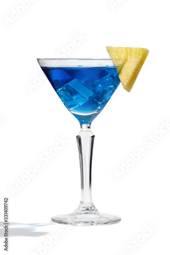 Blue Lagoon cocktail with ice cubes is contained in a martini glass with pineapple slice on the rim. The showy illustrative picture is made on the white background.