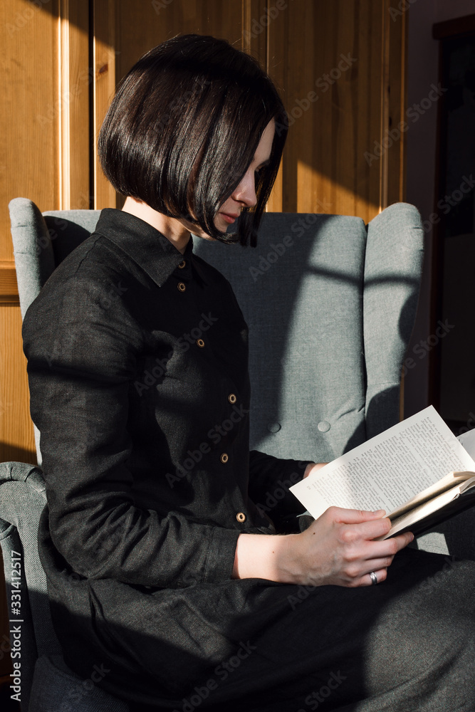 Obraz premium Portrait of young adult woman sitting in a chair and reading books, slow living or leisure concept. selective focus