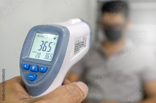 Hand holding infrared thermometer to measuring temperature on blurred asia people with face mask on background. Covid flu screening 19 concept. photo