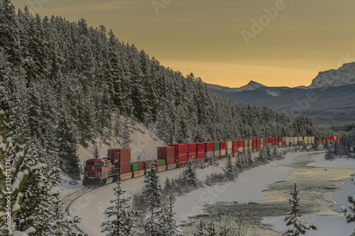 Photo Freight train with containers after picturesque Morant's curve on a cold winter evening with sun just setting behind majestic mountains