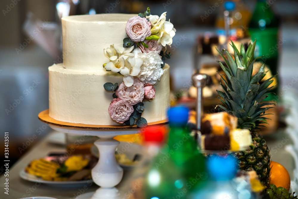 Tall sweet wedding cake decorated with live pink and white flowers on a table.