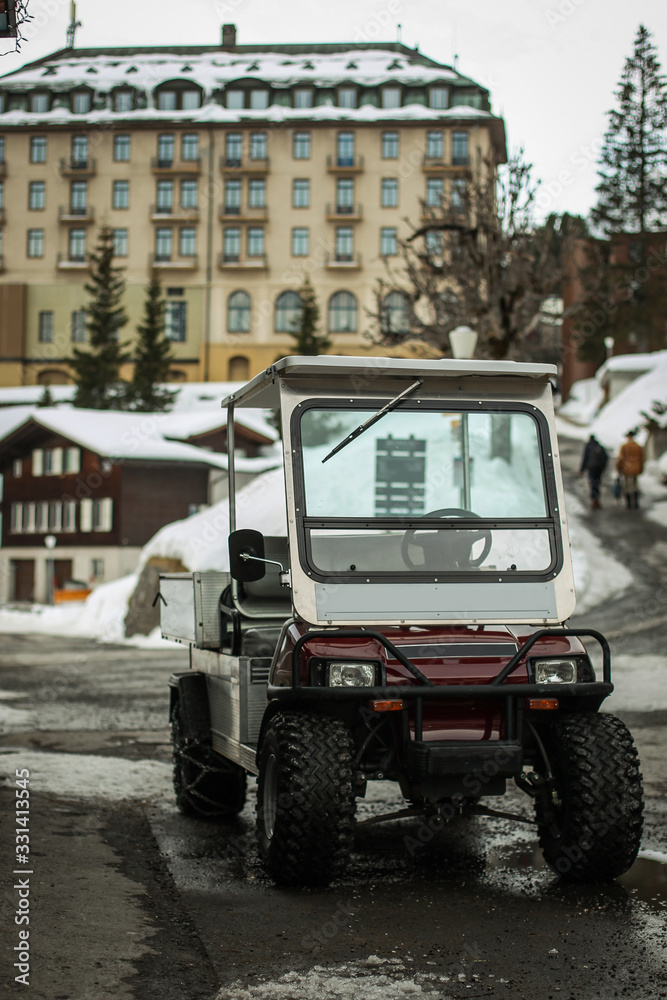 Transport golf cart with snow chains parked in front of a hotel in the Murren region of Switzerland. snow setting in a mountain village.