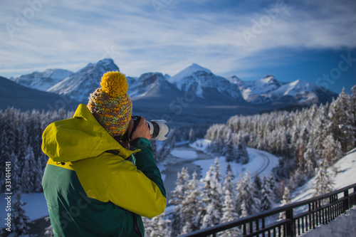 A Man is photographing beautiful snowy mountain scenery. Man in winter clothes and telephoto lens taking pictures of a beautiful mountain landscape. Picture from side and back. photo