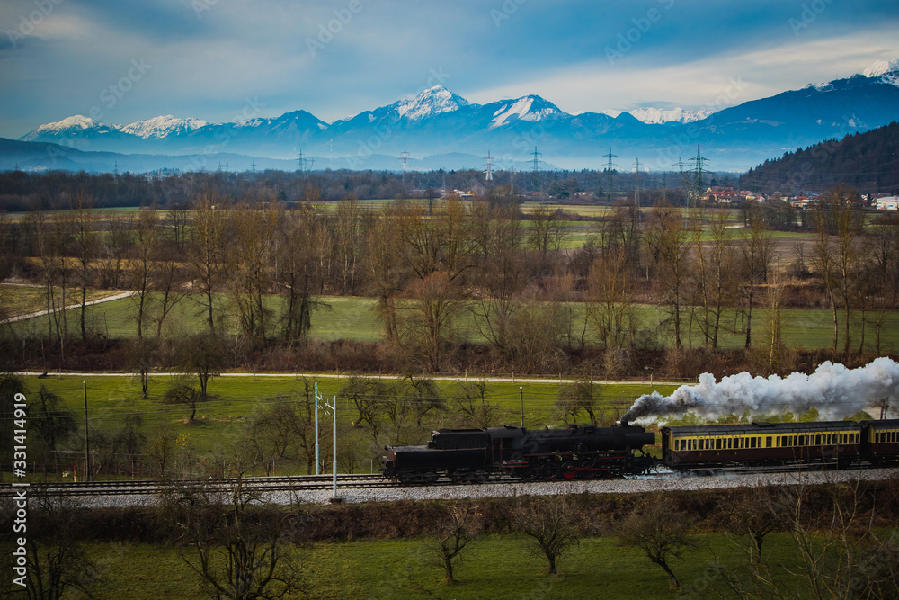 Old vintage steam train is running with loco reversed through the fields with magnificent mountanious terrain in background.