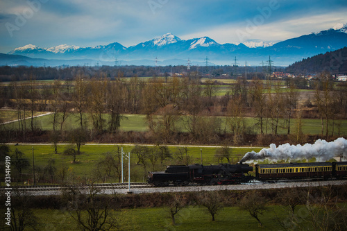 Old vintage steam train is running with loco reversed through the fields with magnificent mountanious terrain in background. photo