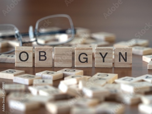 ob gyn concept represented by wooden letter tiles on a wooden table with glasses and a book
