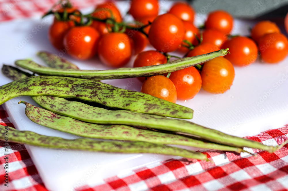 A bunch of cherry tomatoes on cutting board next to green beans.