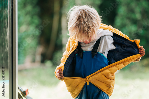 Kleinkind in Regenhose zieht seine Jacke aus