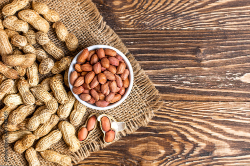 Peanuts in a shell and cleaned in a bowl on a sackcloth on a wooden background. Copy space, top view