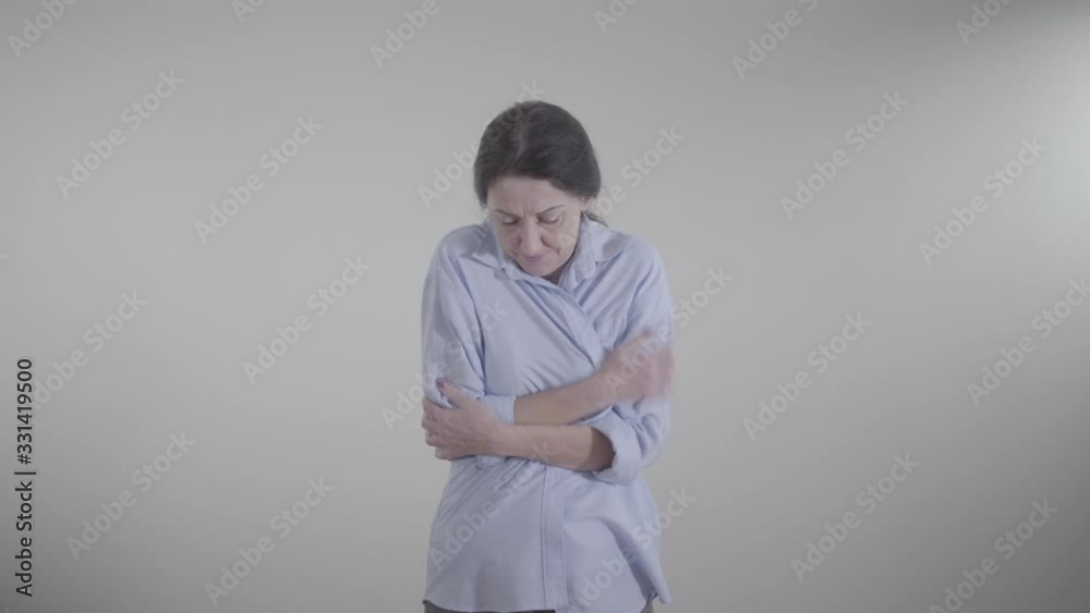 Middle shot of displeased Caucasian woman wrapping herself up and rubbing hands. Portrait of freezed brunette lady suffering from cold temperature indoors.