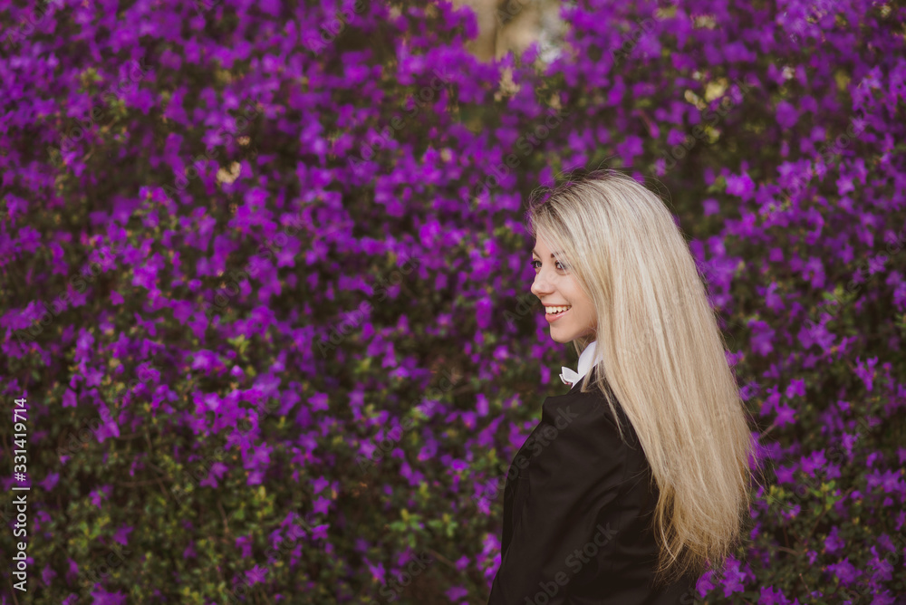 Portrait of an attractive blonde smiling girl in a shirt and jacket against a background of purple blooming flowers Portrait of an attractive blonde smiling girl in a shirt and jacket against a background of purple blooming flowers
