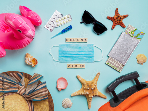Coronavirus covid-19 and travel concept. Summer vacation and beach rest symbols and breathing mask with wood letters coronavirus on blue background. Flat lay or top view.