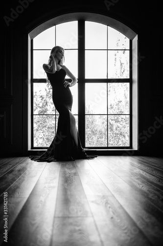 Gorgeous blonde in a black tight-fitting dress in contrast to the window with the frame. Black and white