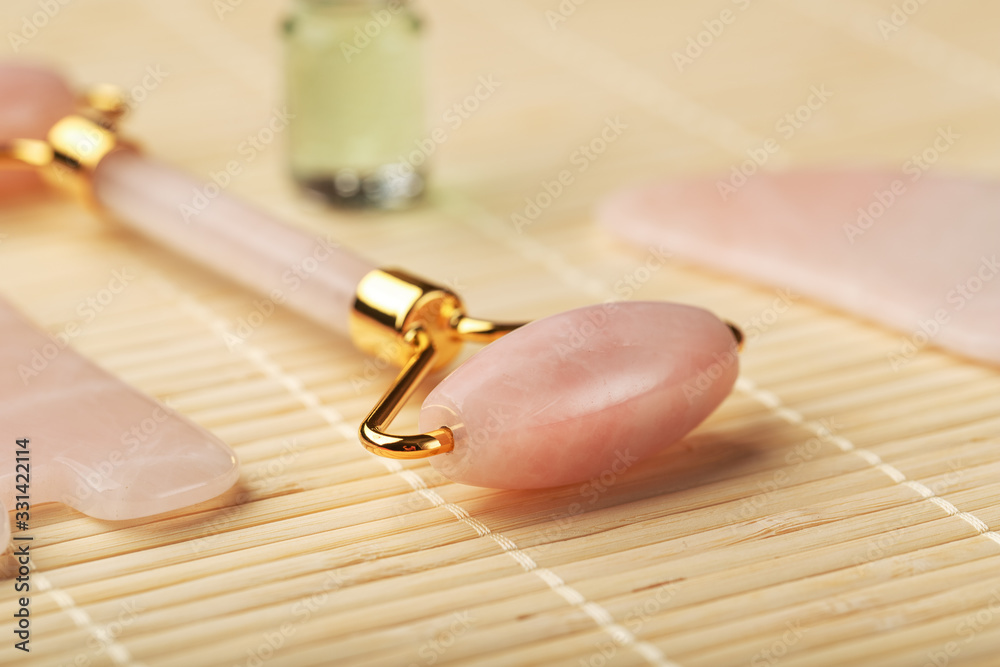 A set of tools for face Massage technique Gua Sha made of natural rose quartz. Roller, jade stone and oil in a glass jar, on a straw background for face and body care. A set of tools for face Massage technique Gua Sha made of natural rose quartz. Roller, jade stone and oil in a glass jar, on a straw background for face and body care.