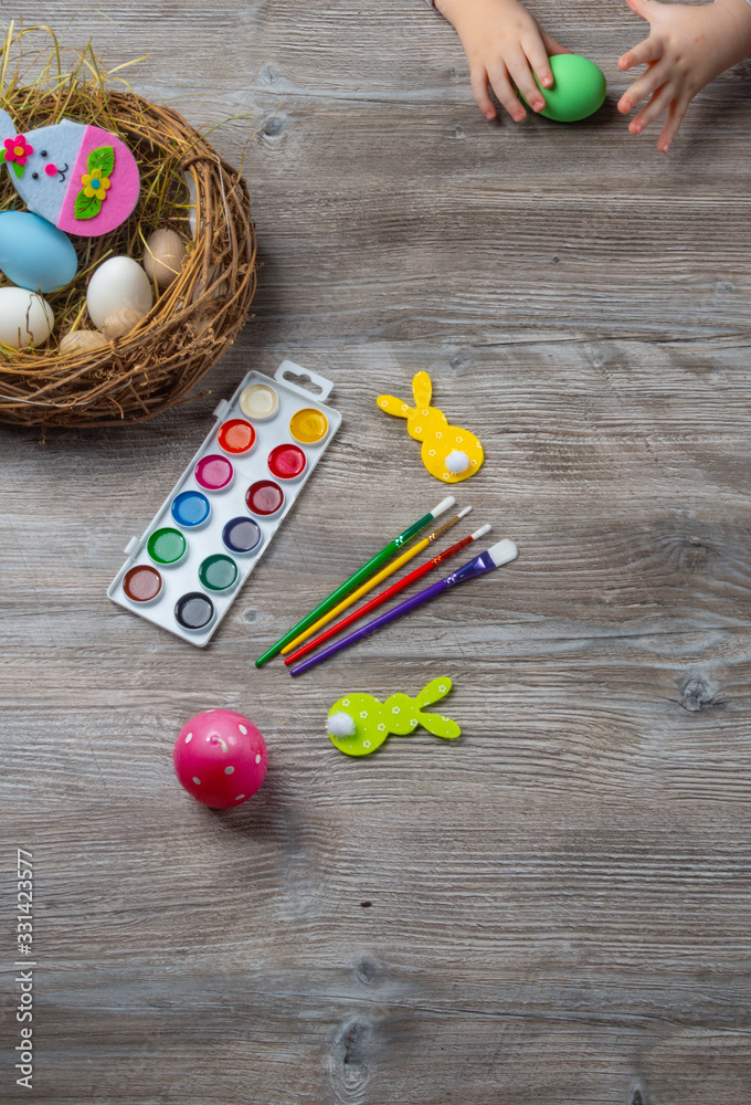 baby hand turn easter egg. In wooden table paints, brushes, bunny, nest baby hand turn easter egg. In wooden table paints, brushes, bunny, nest