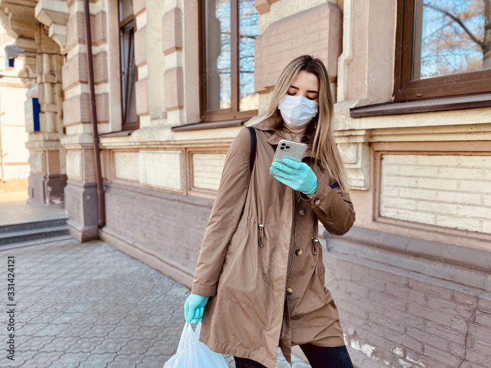 Fototapeta premium girl in a protective mask and gloves against coronavirus in a pharmacy. smartphone in hand. Covid 2019. Covid 2020.