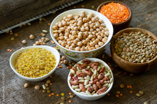 Diet and healthy eating concept, vegan protein source. Raw of legumes (chickpeas, red lentils, canadian lentils, beans, bulgur) on wooden table.