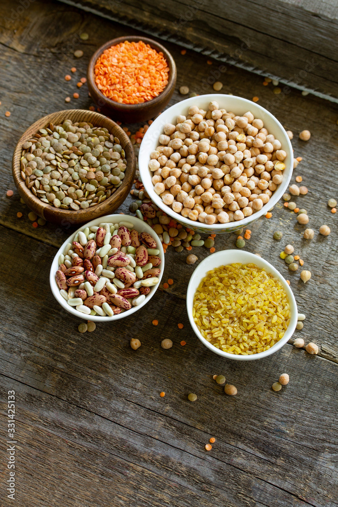 Diet and healthy eating concept, vegan protein source. Raw of legumes (chickpeas, red lentils, canadian lentils, beans, bulgur) on wooden table. Copy space. Diet and healthy eating concept, vegan protein source. Raw of legumes (chickpeas, red lentils, canadian lentils, beans, bulgur) on wooden table. Copy space.