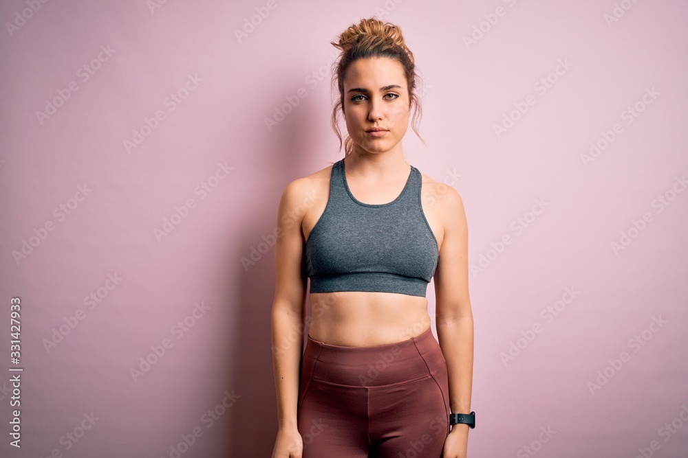 Young beautiful blonde sportswoman doing sport wearing sportswear over pink background Relaxed with serious expression on face. Simple and natural looking at the camera.