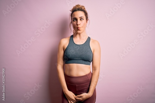 Tableau sur toile Young beautiful blonde sportswoman doing sport wearing sportswear over pink background making fish face with lips, crazy and comical gesture