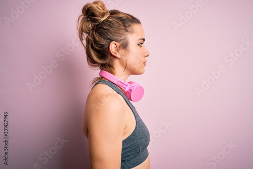 Young beautiful blonde sportswoman wearing sportswear listening to music using headphones looking to side, relax profile pose with natural face with confident smile.