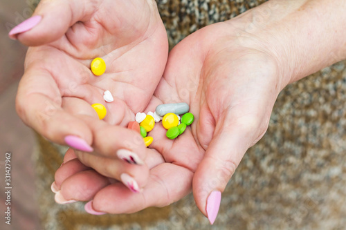 Senior woman holds multicolored different size pills in her hands, hands with manicure. The concept of caring for the elderly