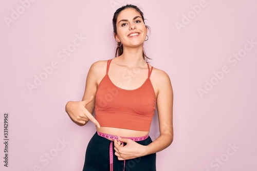 Young beautiful fitness woman wearing sport excersie clothes using measuring tape very happy pointing with hand and finger © Krakenimages.com