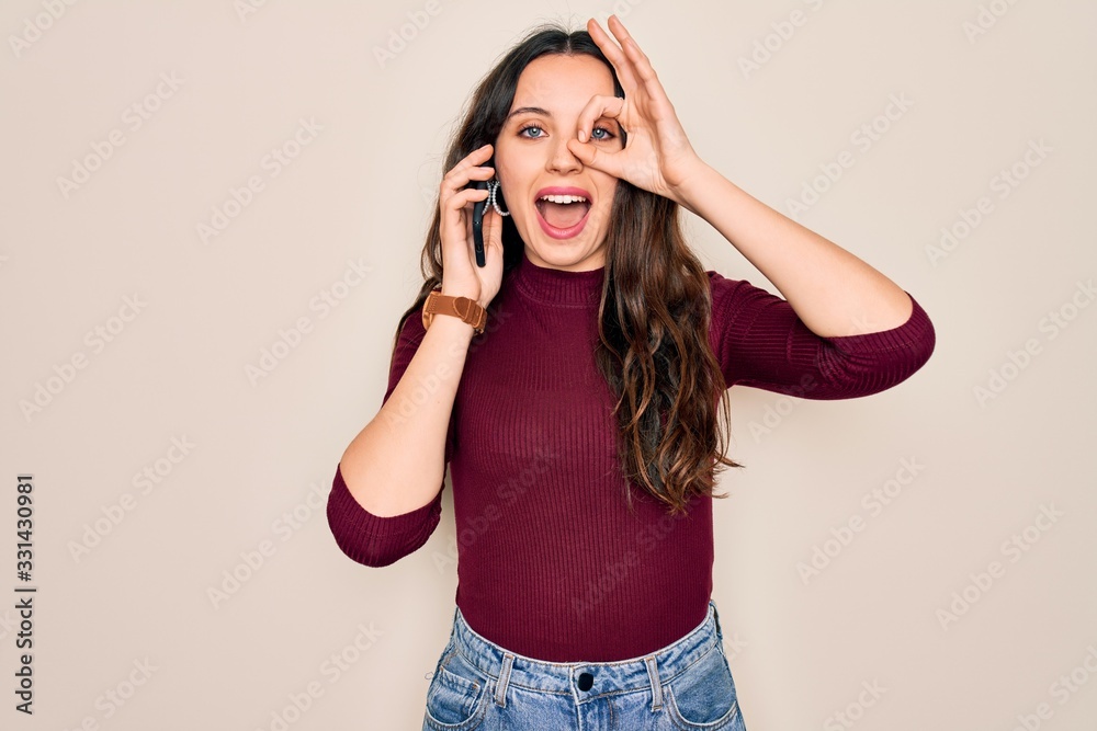 Young beautiful woman having conversation talking on the smartphone over white background with happy face smiling doing ok sign with hand on eye looking through fingers Young beautiful woman having conversation talking on the smartphone over white background with happy face smiling doing ok sign with hand on eye looking through fingers