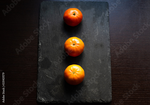 Group of three tangerines on a slate plate and a dark wooden background