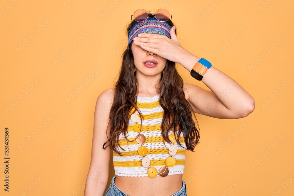 Young beautiful hippie woman with blue eyes wearing accesories and sunnglasses covering eyes with hand, looking serious and sad. Sightless, hiding and rejection concept Young beautiful hippie woman with blue eyes wearing accesories and sunnglasses covering eyes with hand, looking serious and sad. Sightless, hiding and rejection concept