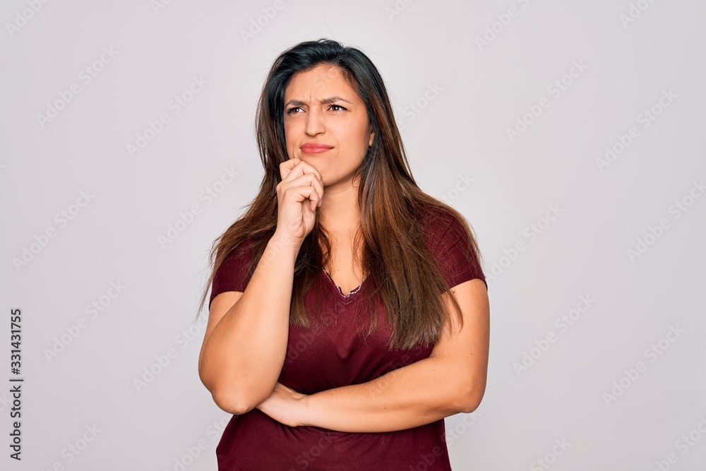 Young hispanic woman wearing casual t-shirt standing over isolated background with hand on chin thinking about question, pensive expression. Smiling with thoughtful face. Doubt concept. Young hispanic woman wearing casual t-shirt standing over isolated background with hand on chin thinking about question, pensive expression. Smiling with thoughtful face. Doubt concept.