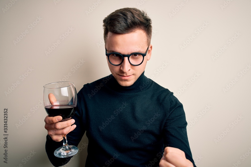 Young handsome caucasian man drinking an alcoholic glass of red wine over isolated background annoyed and frustrated shouting with anger, crazy and yelling with raised hand, anger concept Young handsome caucasian man drinking an alcoholic glass of red wine over isolated background annoyed and frustrated shouting with anger, crazy and yelling with raised hand, anger concept