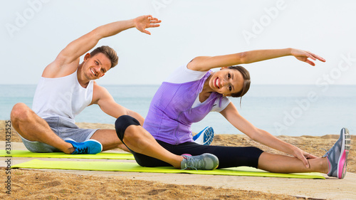 Young couple training yoga poses sitting on beach