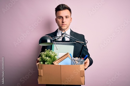 Young handsome caucasian business man holding cardboard box unemployment fired from job with a confident expression on smart face thinking serious photo