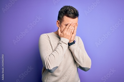 Young handsome caucasian man wearing casual sweater over purple isolated background with sad expression covering face with hands while crying. Depression concept.