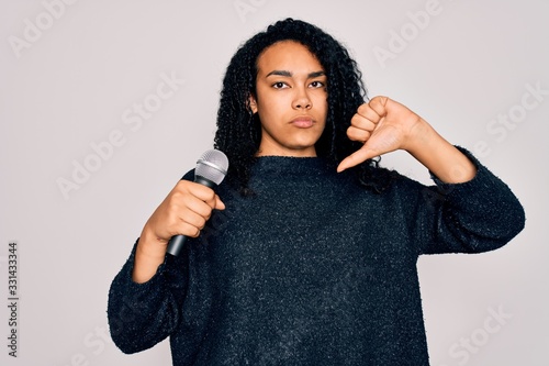 Young african american curly singer woman singing using microphone over white background with angry face, negative sign showing dislike with thumbs down, rejection concept