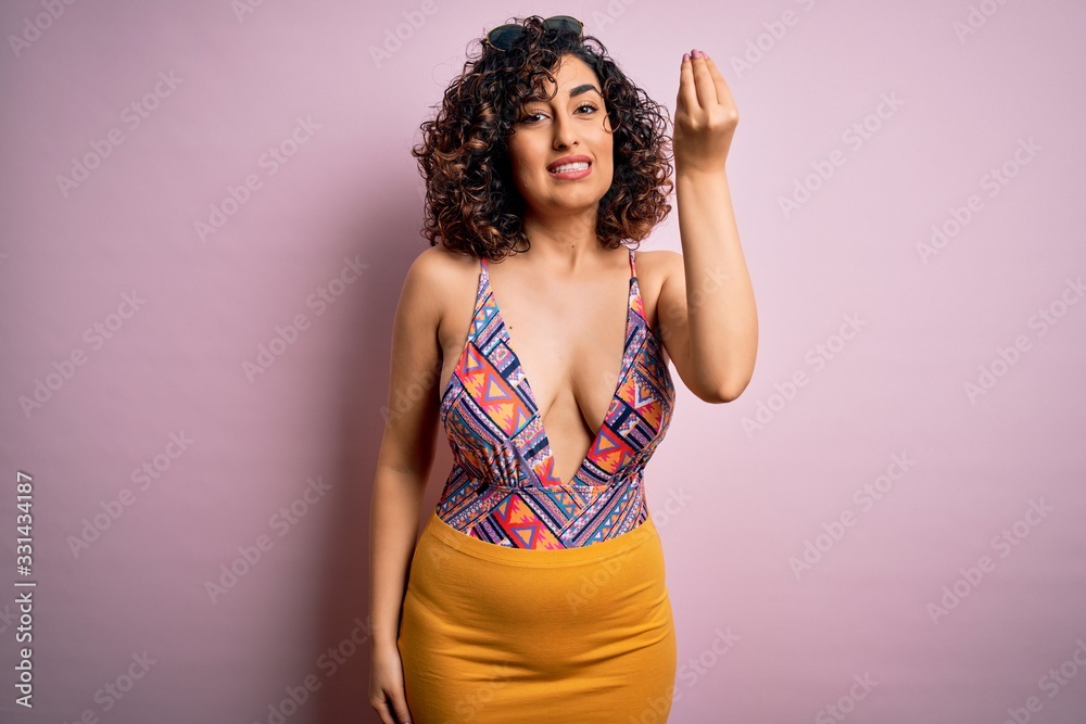Young beautiful arab woman on vacation wearing swimsuit and sunglasses over pink background Doing Italian gesture with hand and fingers confident expression Young beautiful arab woman on vacation wearing swimsuit and sunglasses over pink background Doing Italian gesture with hand and fingers confident expression