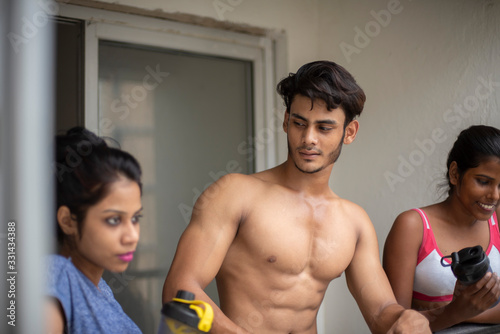 An young Indian Bengali group of friends/siblings are enjoying themselves standing on the balcony after work out in white background. Indian lifestyle.