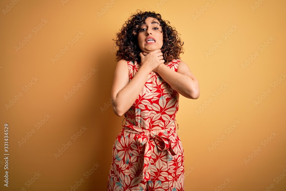 Young beautiful curly arab woman on vacation wearing summer floral dress and sunglasses shouting and suffocate because painful strangle. Health problem. Asphyxiate and suicide concept.