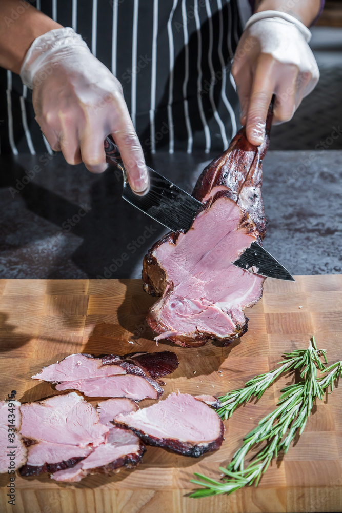 A cook cuts a smoked lamb leg into slices on a wooden cutting board
